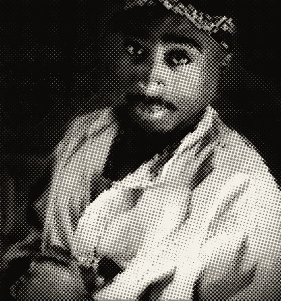 Black and white portrait of Tupac Shakur in a bandana, arms crossed, looking straight into the camera.