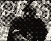 Tupac in a bandana in front of a wall covered in graffiti.
